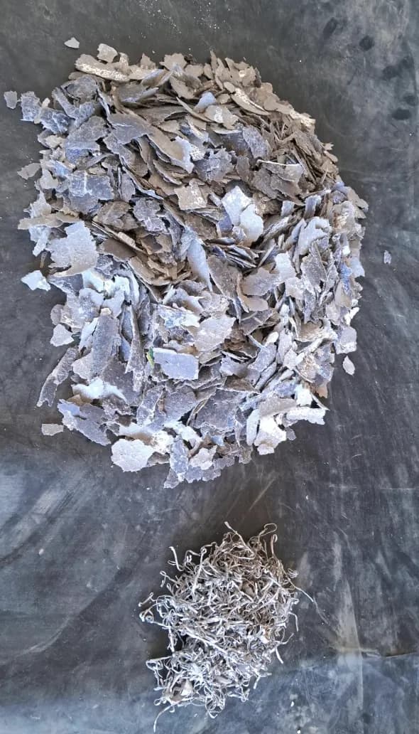 Monte de fragmentos acinzentados de células de silício separados na reciclagem, com um pequeno monte de fitas metálicas finas e retorcidas logo abaixo
