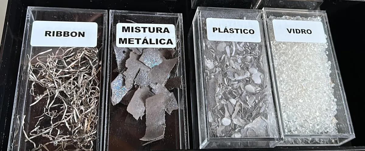 Caixa de acrílico aberta com quatro compartimentos de amostras recicladas rotulados ribbon, mistura metálica, plástico e vidro