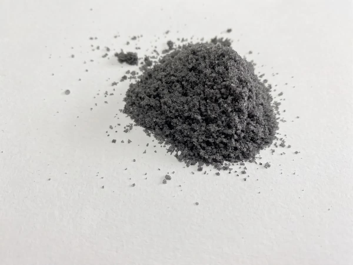 Pequeno monte de material granulado cinza escuro sobre fundo branco: a mistura de plástico, silício e metais que sai do laminado do painel solar na reciclagem