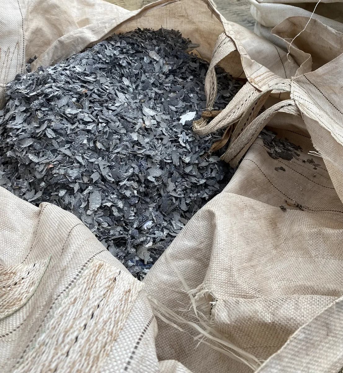Big bag aberto cheio de fragmentos escuros de laminado de módulo fotovoltaico, a mistura de plástico, silício e metais chamada PMM