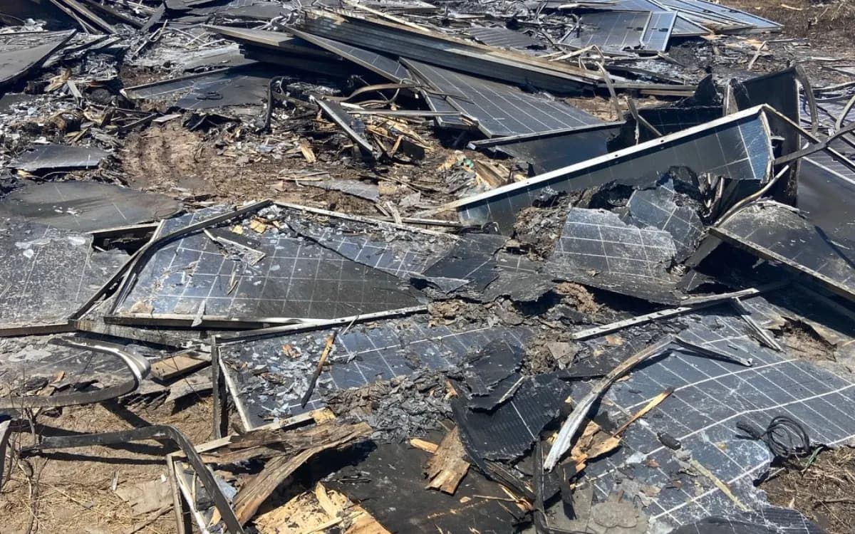 Módulos fotovoltaicos queimados e retorcidos depois de um incêndio em usina, com vidro estilhaçado, molduras de alumínio deformadas e restos de madeira carbonizada sobre o solo