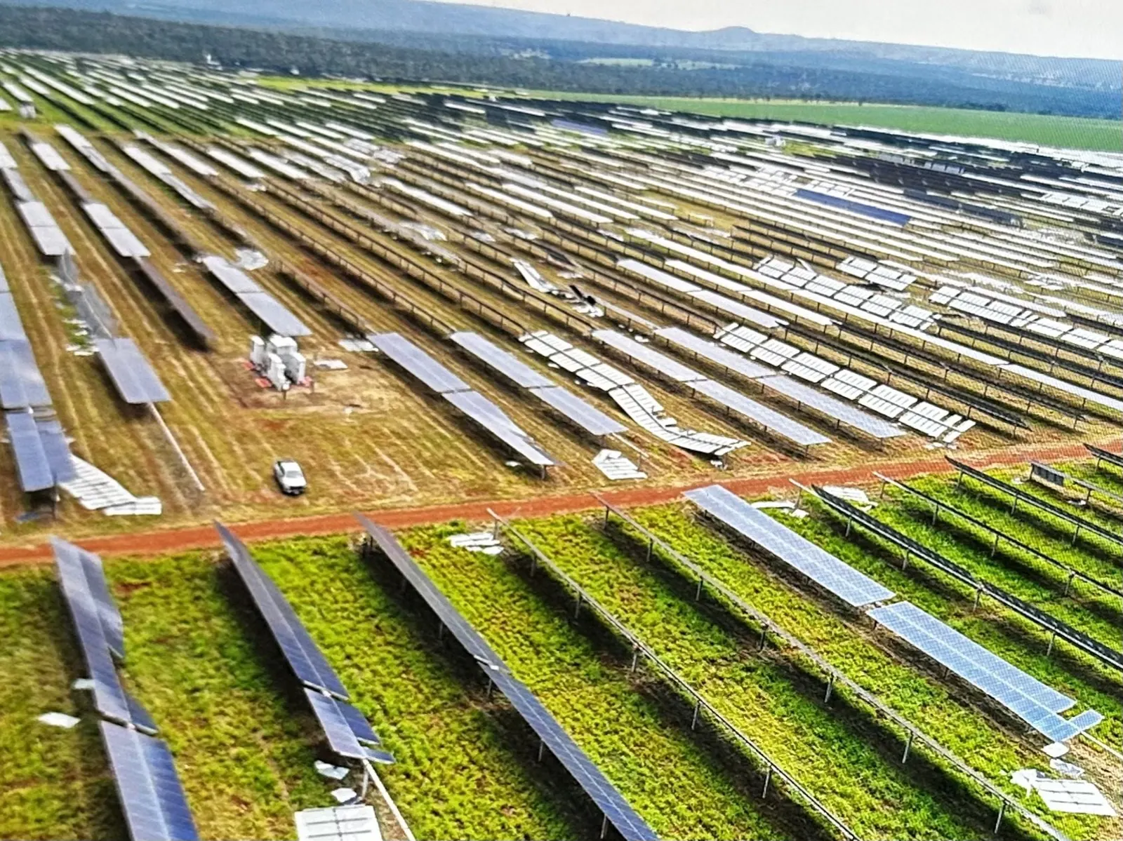 Vista aérea de uma usina solar extensa, com parte das fileiras de módulos danificadas e estruturas desalinhadas no meio de mesas ainda intactas